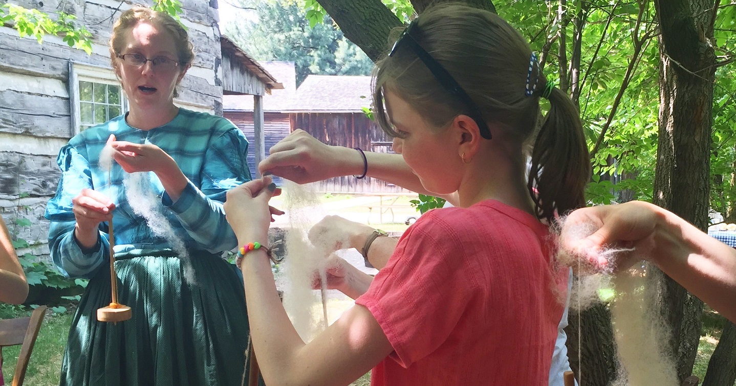 young visitor to the Village at Black Creek learns traditional 19th century method of working with wool from costumed educator in Victoria dress