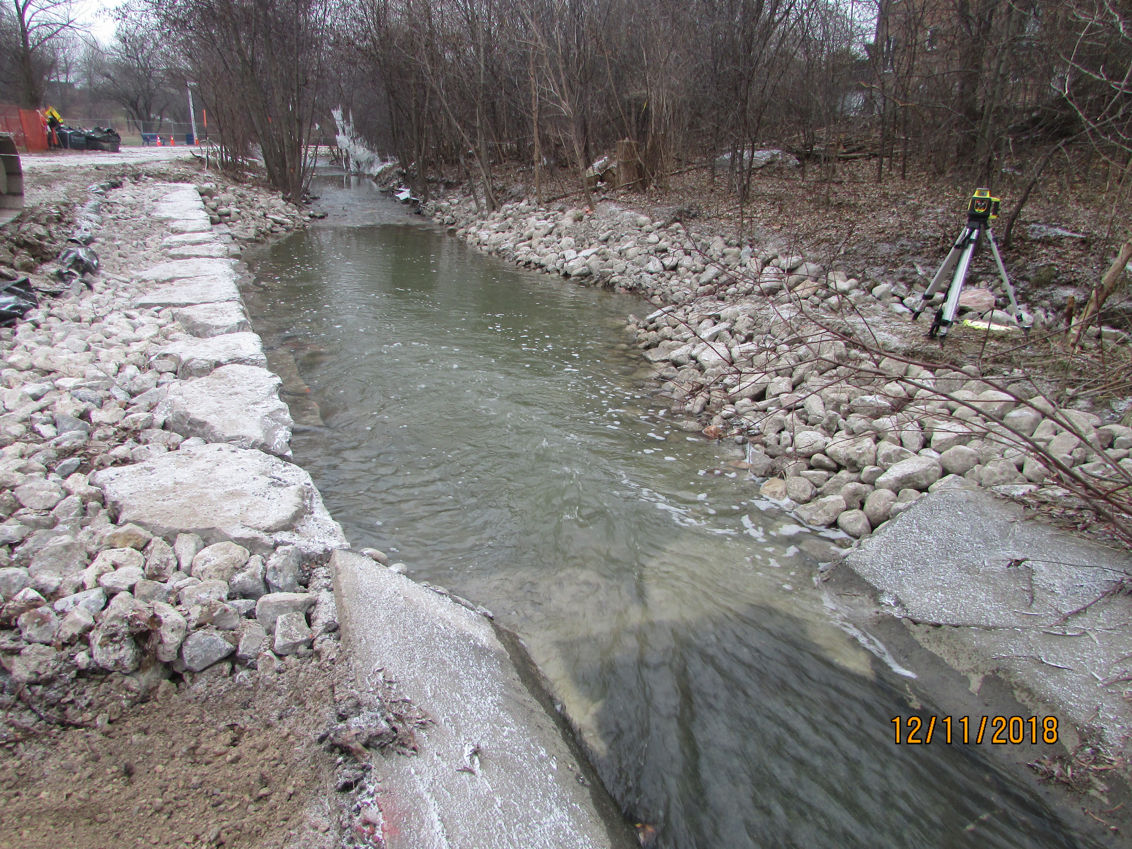 Photo of a single-tier armourstone wall on the left bank of Etobicoke Creek with a cobblestone channel on the right bank of the Creek. A preexisting concrete channel is located further upstream.