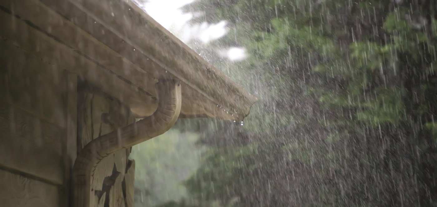 heavy rain falls on the gutters and downspout of an old house