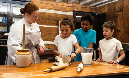 a costumed educator at The Village at Black Creek teaches summer campers how to churn butter