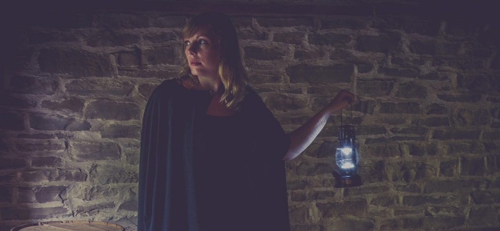 a guide wearing a black robe and carrying a lantern leads a ghost tour of The Village at Black Creek