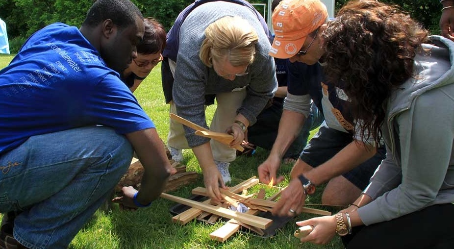 a group of adults work together to build a fire during a team challenge day at the Nature Centre at Bruces Mill