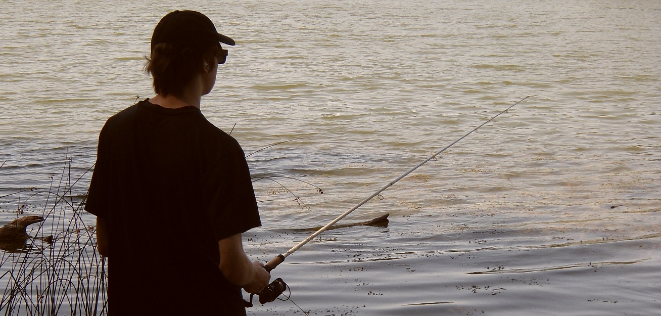 a young man enjoys fishing on a summer evening at Heart Lake Conservation Park