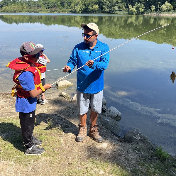 a TRCA Learn to Fish instructor shows a young angler how to use a fishing rod