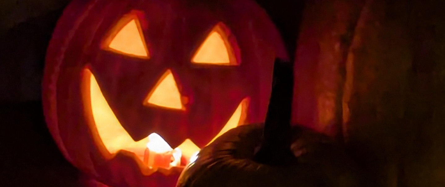 the grinning illuminated face of a Halloween jack-o-lantern in the dark
