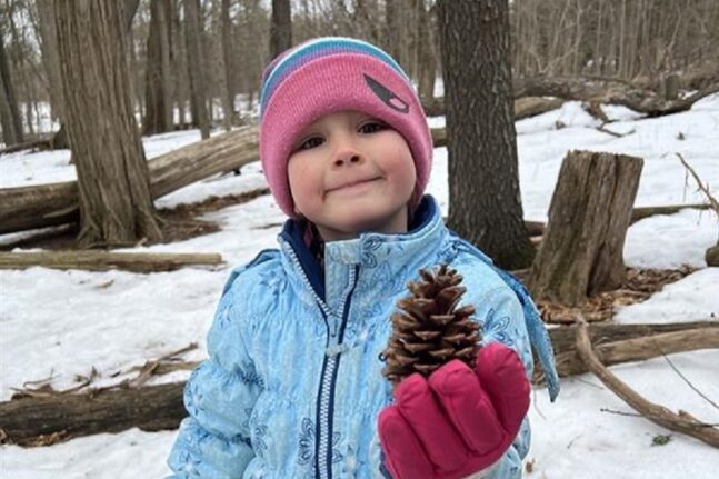 a student holds up a pine cone at a March Break camp at Lake St George Field Centre