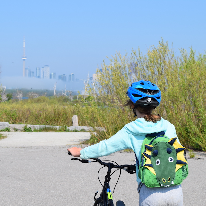 a summer camper views the Toronto skyline from a trail at Tommy Thompson Park