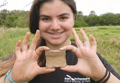 a high school student holds up a fragment unearthed at the Boyd Archaeological Field School