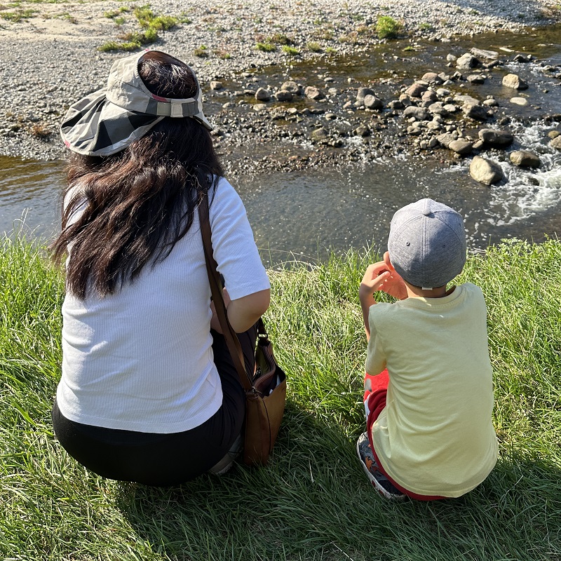 a mother and son sit on the grass overlooking Highland Creek at the TRCA Adventures of Salmon event