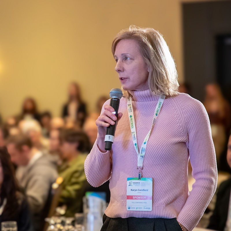 an audience member holding a microphone asks a question of a speaker at the Source to  Stream Conference