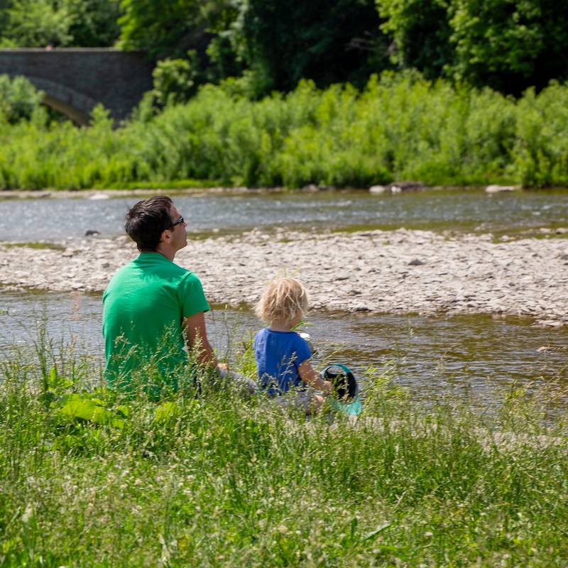 a father and son sitting on the grass in Etienne Brule Park enjoy a view of the Humber River