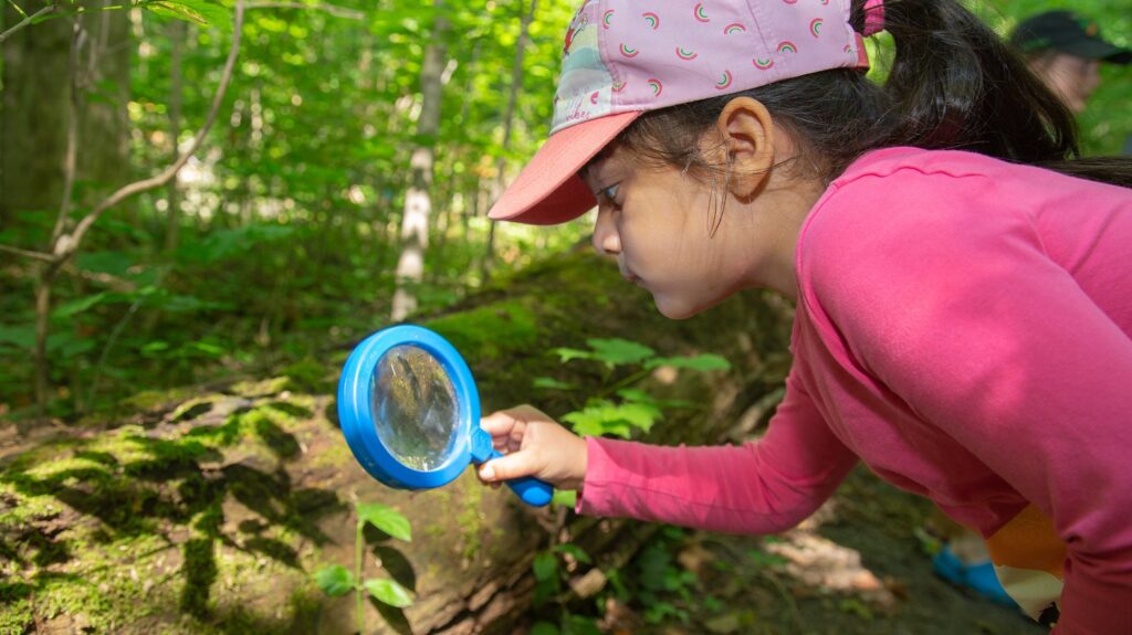 a summer camper uses a magnifying glass to study moss on a log at Claireville Outdoor Education Centre