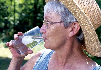 a woman in a sun hat drinks a glass of ice water on a summer day