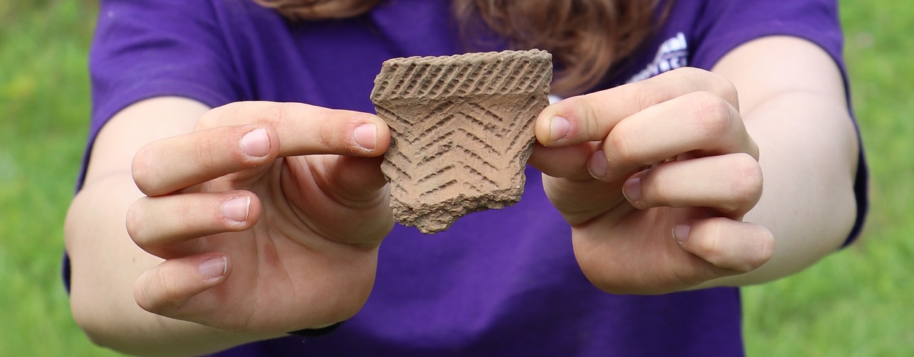 A student at the Boyd Archaeological Field School holds up an artifact uncovered at an excavation site