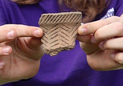 A student at the Boyd Archaeological Field School holds up an artifact uncovered at an excavation site