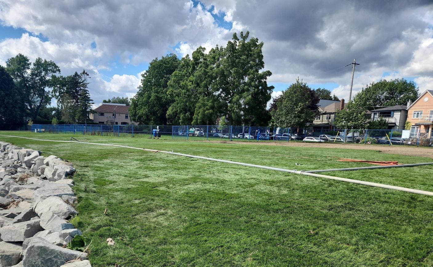The work area is covered in newly installed sod. A PVC pipe has been laid in the middle of the lawn. The erosion control treatment is visible on the left and the construction fence is shown on the right.