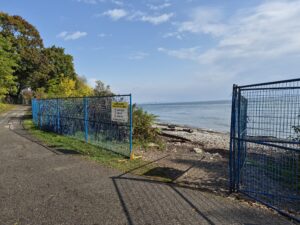 An open construction fence leads to the a cobble shoreline.